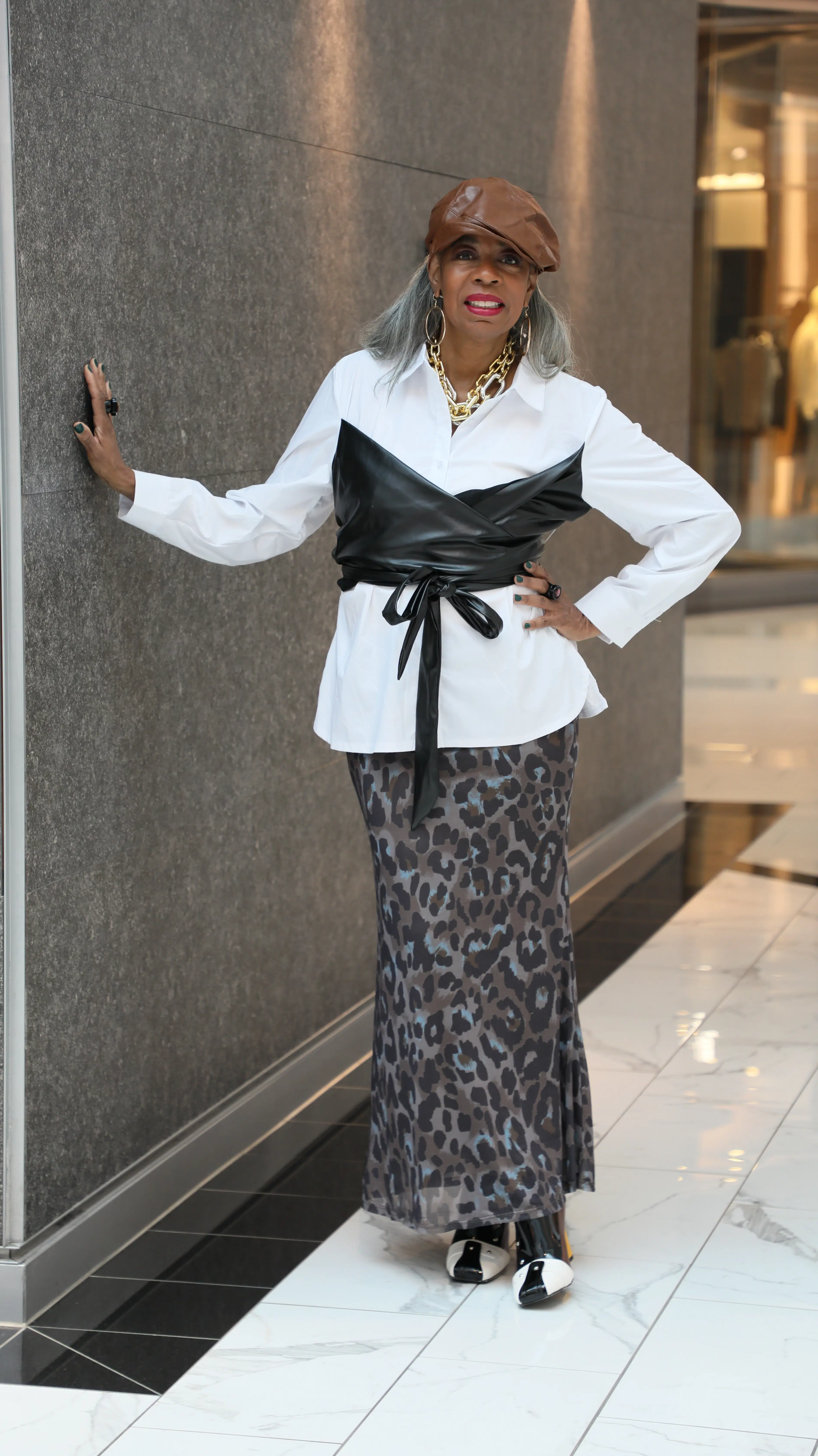 Dorris Burch wearing a brown leather cap, white shirt, black leather corset belt, and leopard-print skirt